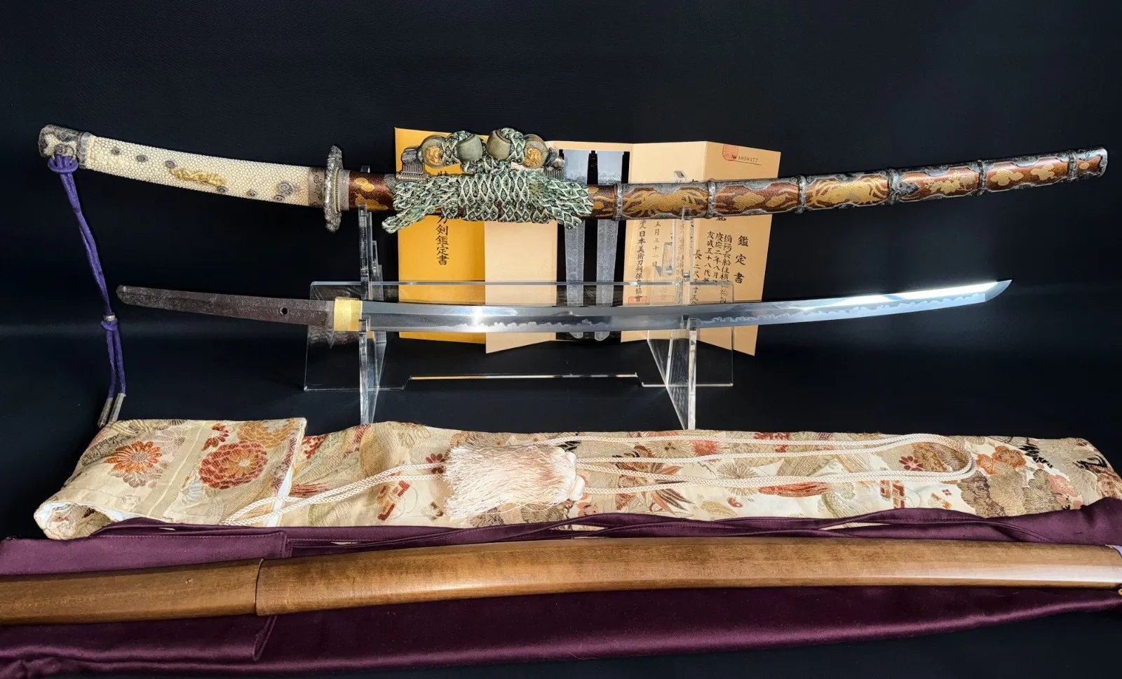 Antique Japanese tachi displayed with its polished blade on a stand, gold lacquered koshirae with same wrapped hilt, brocade sword bag, shirasaya and Japanese appraisal papers