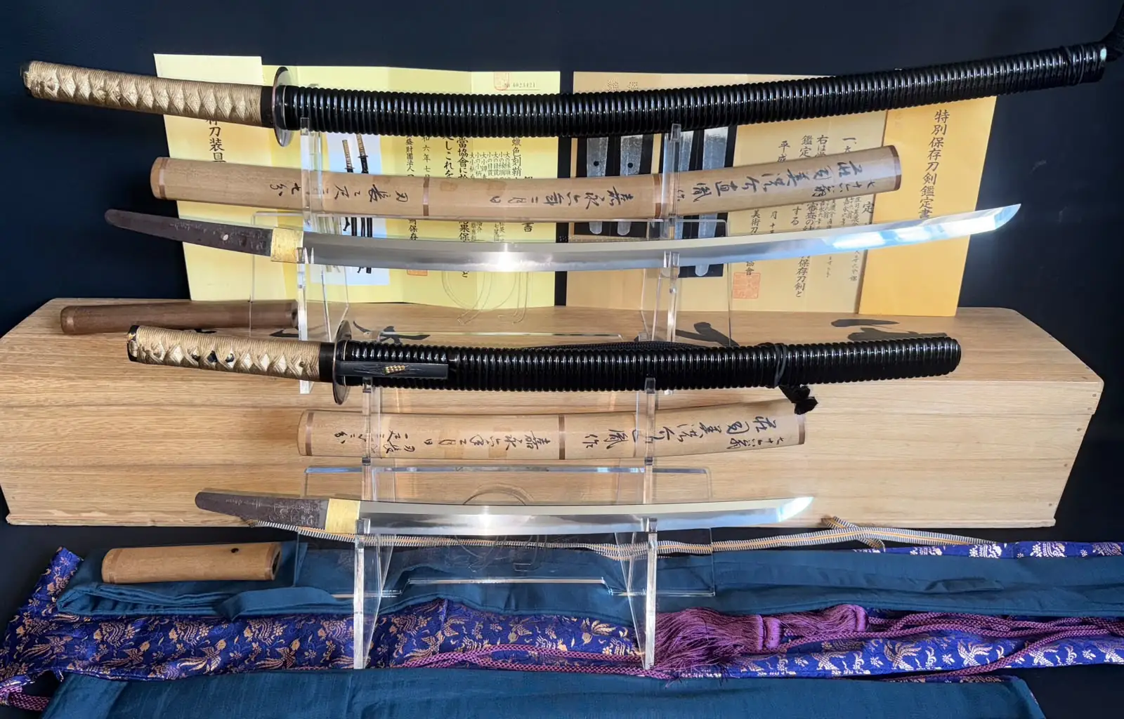 Taikei Naotane Daishō katana and wakizashi drawn from their shirasaya, blades resting on acrylic stands in front of NBTHK Tokubetsu Hozon and NBTHK Hozon koshirae certificates
